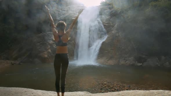 Woman Stands in Yoga Position Against Waterfall