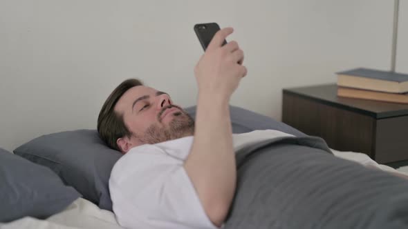 Young Man Using Smartphone While Laying in Bed
