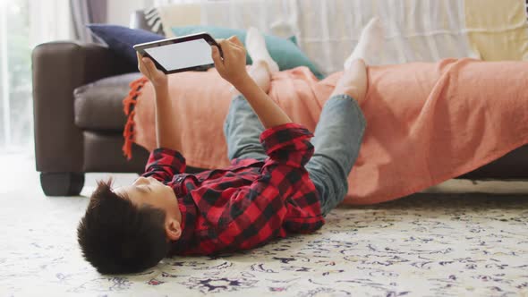 Happy asian boy at home, lying on floor in living room using tablet