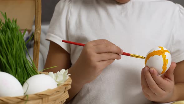 A young child prepares for the religious holiday of Easter by painting eggs with paint.