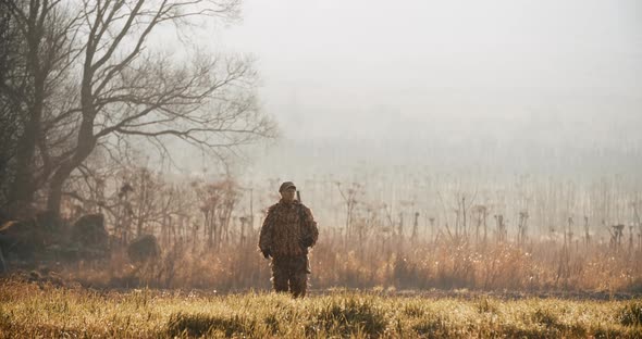 Hunter in hunting equipment with rifle on his shoulder walks through on camera in the field