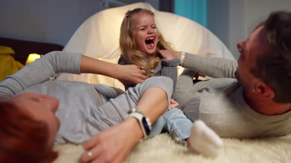 Portrait of Laughing Cute Little Girl Having Fun with Parents Tickling Daughter Lying at Tent in