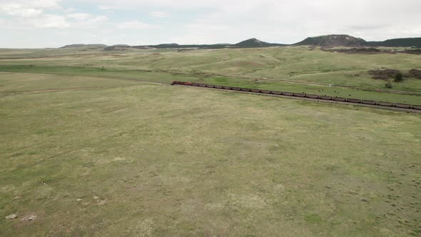 Aerial approach towards end of long coal train moving through open farmland.