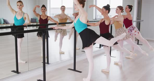 Caucasian ballet female dancers exercising together with a barre by a mirror during a ballet class
