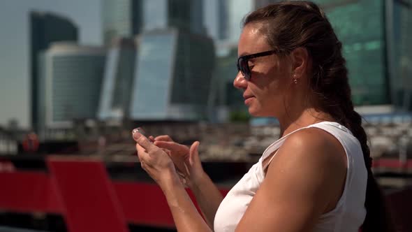 Portrait of a Woman with Dark Glasses and Long Braids on the Background of High-rise City Buildings