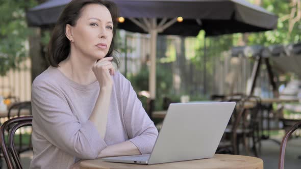 Pensive Old Woman Thinking while Working Outdoor on Laptop