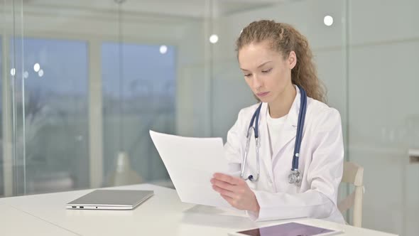 Hardworking Young Female Doctor Reading Documents in Office