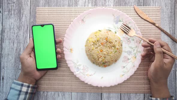 Young Man Hand Holding Smart Phone and Eating Cooked Rice