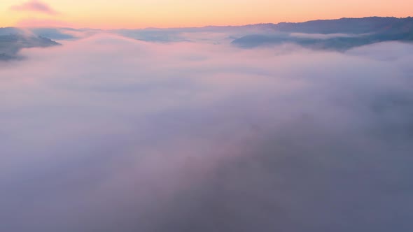 4K aerial view over mountain at sunrise in heavy fog. golden morning sunlight