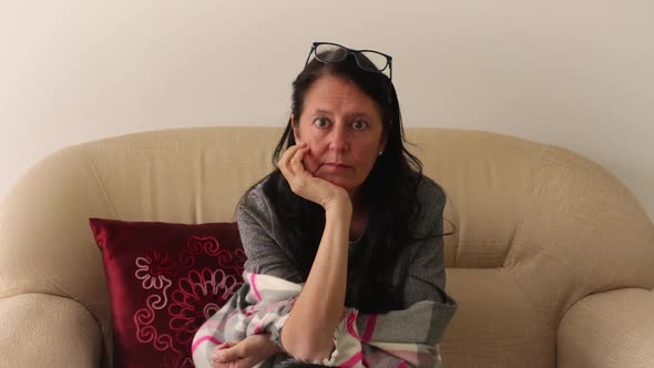 Middle-aged woman seated in double armchair looking at her surrounds with bored expression.