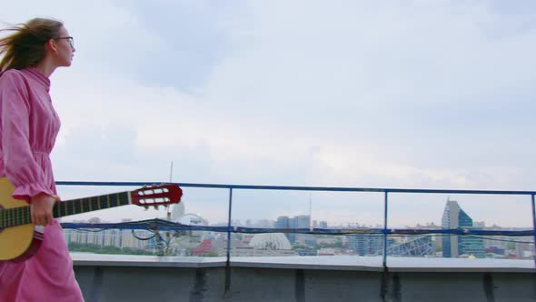 A Woman is Walking on the Roof with a Guitar