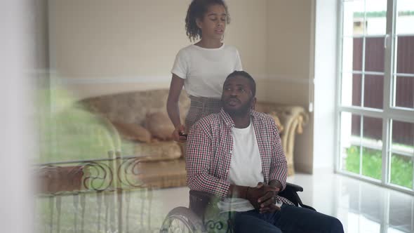 Shooting Through Window Glass African American Father in Wheelchair and Teenage Daughter Talking in