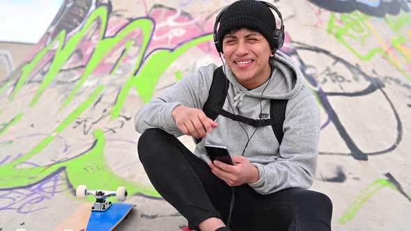 Young Latin Man Skateboarder, with Mobile Phone, Texting at Skate Park