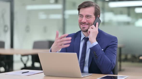 Hardworking Young Businessman with Laptop Talking on Smartphone