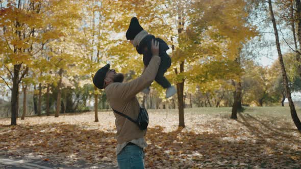 Father Raises His Son to the Sky in the Yellow Autumn Park on a Sunny Day