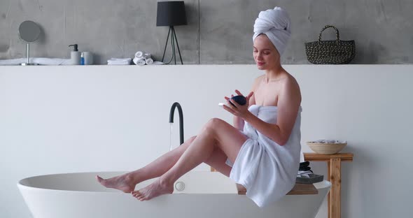 Halfnaked Beautiful Woman Wrapped in White Bath Towels Applies Moisturizer to Her Legs Makes a
