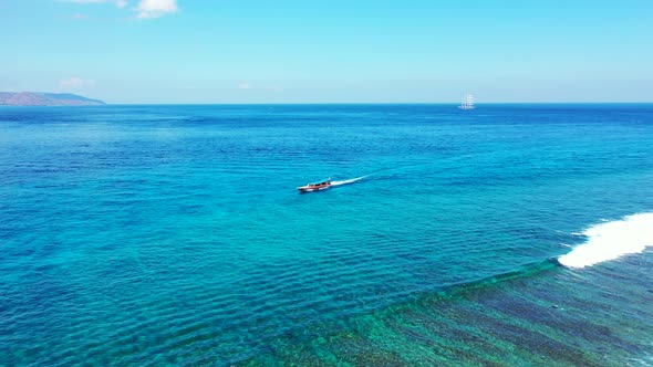 Tourist boat sailing alongside beautiful shoreline of tropical island on calm clear water of turquoi