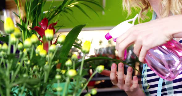 Female florist spraying water on flowers in flower shop