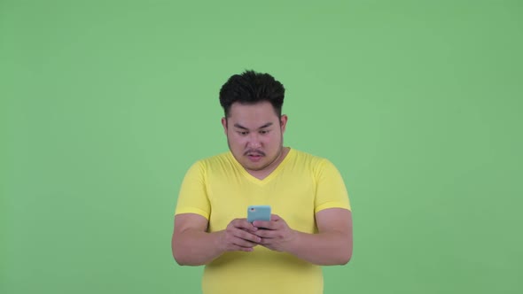 Face of Happy Young Overweight Asian Man Using Phone and Looking Surprised