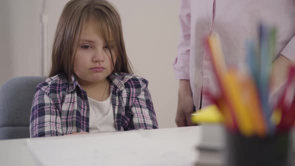 Portrait of Little Caucasian Schoolgirl Sitting at the Table with Upset Facial Expression As Her