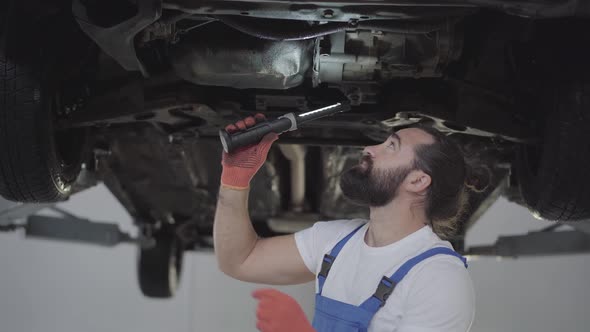 Successful Bearded Mechanic Inspecting Suspension or Brakes in Car