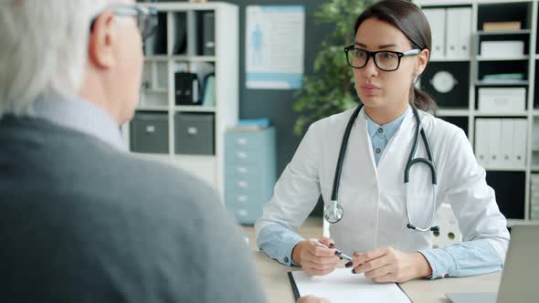 Young Woman Doctor Shaking Hands with Elderly Man Patient Talking in Office