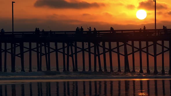 People walking across pier during colorful sunset