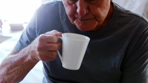 Senior man sitting on bed and having cup of coffee