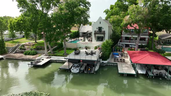 Aerial pullback reveal of waterfront homes on lake with boat dock. Rising shot over lake water.