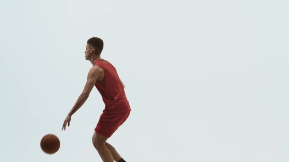 Side View or Young Basketball Player in Red Sports Uniform Runs and Dribbles on White Studio