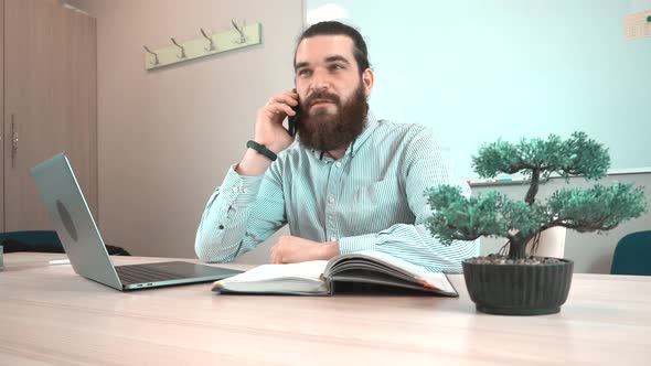 Footage of young bearded man in office talking on smartphone.