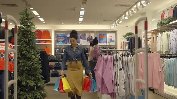 Happy African American Woman with Paper Bags Walks Out of Women's Clothing Store in Mall