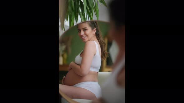 A Pregnant Girl Looks at Her Belly in the Mirror