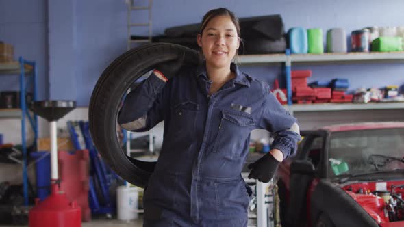 Portrait of female mechanic holding a tire and smiling at a car service station