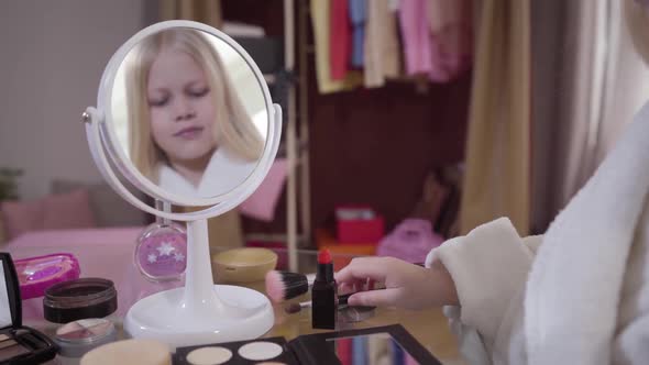 Reflection in Mirror of Little Cute Caucasian Blond Girl Taking Makeup Brush for Applying Eye
