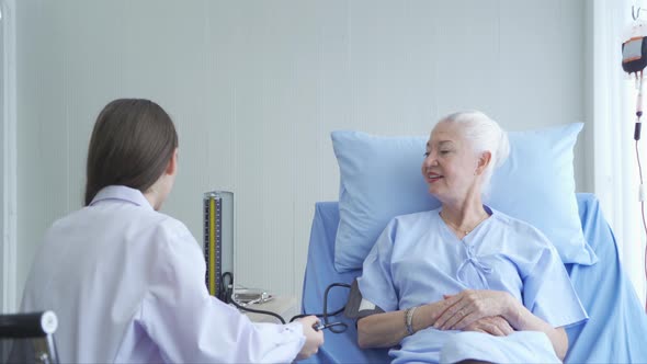 Happy woman doctor checking blood pressure test of sick old female senior elderly patient lying