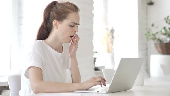 Tired Young Woman Yawning While Working on Laptop