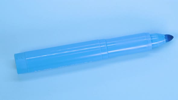 Cyan marker pen rotating on blue surface background, macro shot close up view detail.