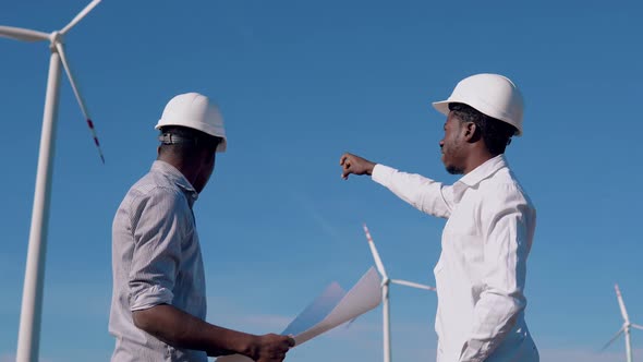 Two Male African American Electrical Engineers Stand in the Background of a Windmill at an Air Power