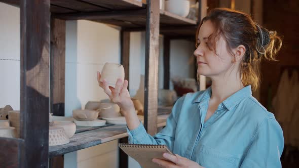 Slow Motion of Serious Female Potter Checking Ceramics and Writing Notes in Workshop