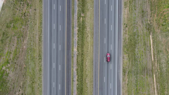 Cars and trucks driving on a divided highway while the camera looks straight down. Vehicles exit and