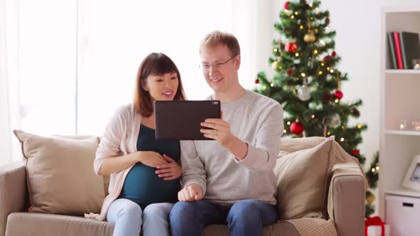 Man and Pregnant Woman with Tablet Pc on Christmas