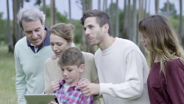 Family using digital tablet together outdoors, looking in awe at something out of frame