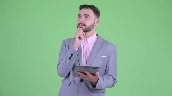 Happy Young Bearded Businessman Thinking While Using Digital Tablet