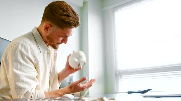 Depressed businessman with beard shakes white piggy bank