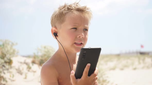 Cute Boy Uses Smartphone on the Beach