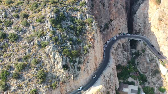 aerial drone panning upwards as cars travel on a coastal road alongside a steep mountain cliff at Ka