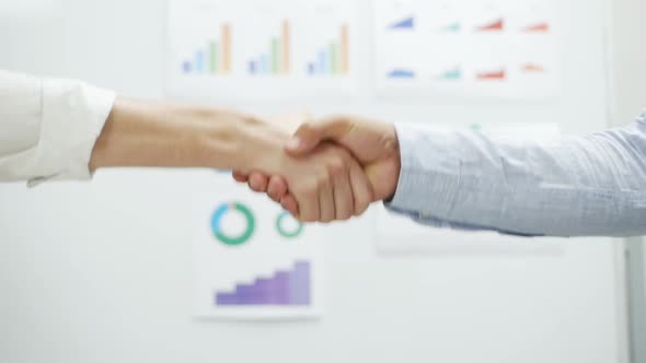 Close-up of Handshake of Two Businessmen, Graphs and Charts in the Background. Deal, Agreement