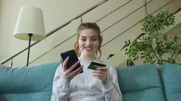 Young Woman Holding Credit Card Using Instant Mobile Payments at Home.