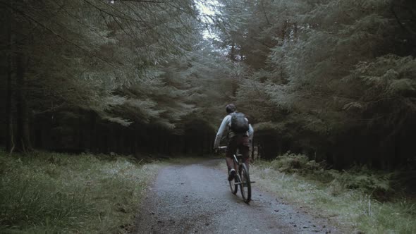 Youth cycles down forest pathway within nature wearing backpack